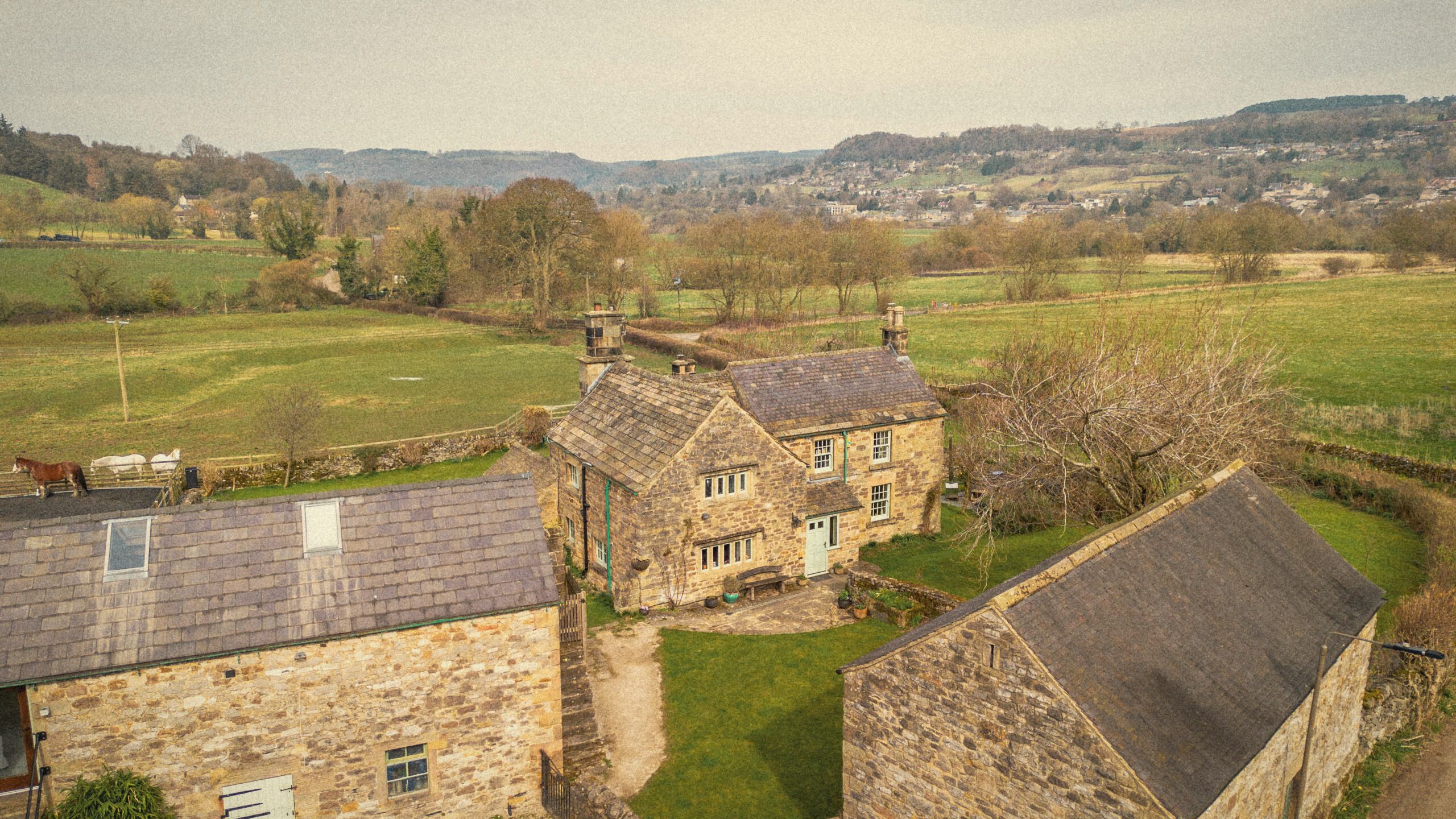 The Old Manor House and its stone outbuildings from the air, with the valley and hills beyond